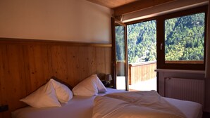 Ein Schlafzimmer mit einem hölzernen Kopfteil, einem großen Fenster mit Blick auf einen Wald und einem Bett mit weißer Bettwäsche.