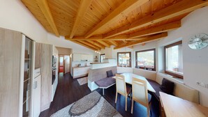 Eine moderne Küche mit Holzbalken, ein Essbereich mit Tisch und Stühlen sowie ein Blick ins Freie durch große Fenster.