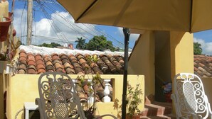 Une terrasse avec deux chaises en métal blanc, une table sur laquelle se trouve un saladier, et des plantes en pot.