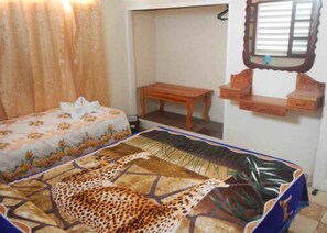 A bedroom with a bed featuring a giraffe print bedspread, a wooden bench, a small table, and a mirror on the wall. - Casa La Fortaleza (Baracoa)