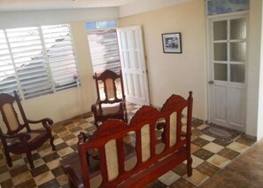 A room with a checkered floor, wooden furniture, a door, and a window with blinds. - Casa La Fortaleza (Baracoa)
