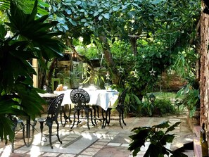 An outdoor patio with a table set for dining, surrounded by lush greenery and a brick wall. - Casa Las Artes (Trinidad)