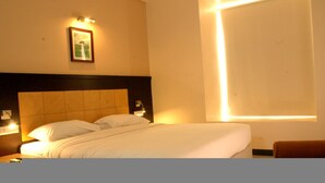 A hotel room with a large bed, a headboard, bedside lamps, a framed picture on the wall, and a window with a light fixture.