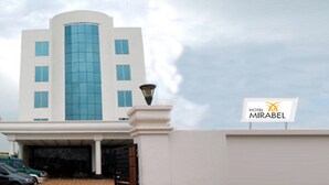 A modern hotel entrance with a large glass facade, a covered parking area, and a sign for Hotel Mirabel.