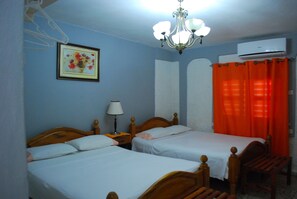 A room with two wooden beds, a chandelier, a framed picture, an air conditioner, and orange curtains. - Casa Micher y Deylin (Viñales)