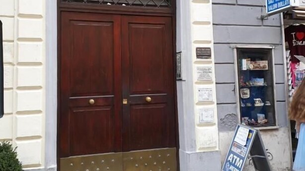 Un edificio con un gran puerta de madera doble, una ventana pequeña con reja metálica y un letrero que indica un cajero automático.