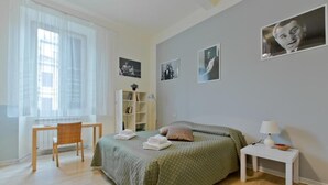 Un dormitorio con cama, escritorio, silla, mesita de noche y ventana.