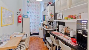 Cocina compacta con microondas, lavamanos y armarios. Hay un extintor de incendios en la pared y un mapa en la puerta.