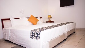 A neatly made bed with a patterned throw, a bedside lamp, and a flat-screen TV on the wall. - Mikaddo City Inn (Kumasi)