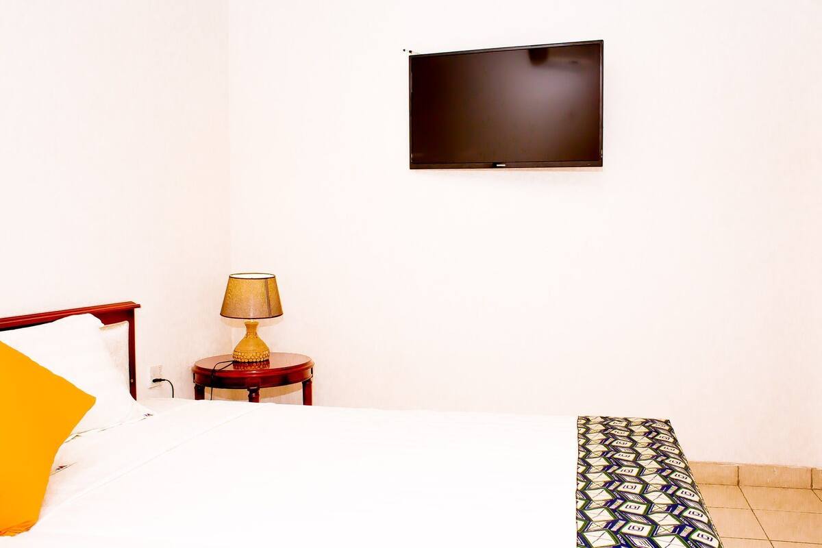 Quarto de hotel com uma cama, uma mesa de cabeceira com abajur e uma televisão de tela plana fixada na parede.