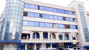 A multi-story building with a glass facade, several storefronts, and a clinic sign. - Mikaddo City Inn (Kumasi)