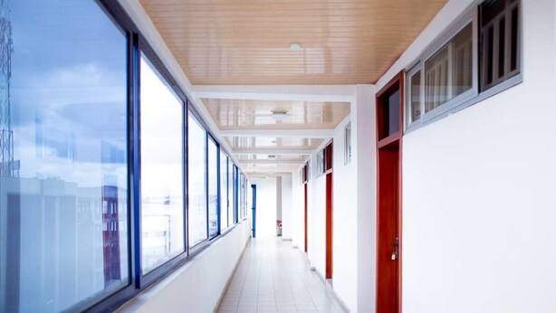 A corridor with large windows, wooden ceiling, and red doors. - Mikaddo City Inn (Kumasi)