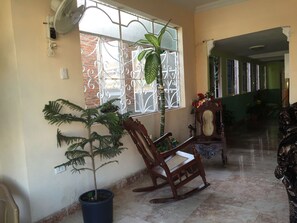 A room with a large window, a potted plant, a rocking chair, and a wooden chair. - Hostal Juan Fernandez (Trinidad)