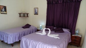 Two twin beds with purple bedding, a nightstand with a lamp, and a decorative wall piece. - Hostal Restaurante La Rosa (Trinidad)