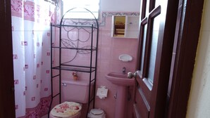A small bathroom with a pink toilet, a sink, a shelf unit, and a shower curtain. - Hostal Restaurante La Rosa (Trinidad)