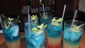 Four glasses of layered drinks with mint leaves and straws, placed on a tray. - Hostal Restaurante La Rosa (Trinidad)