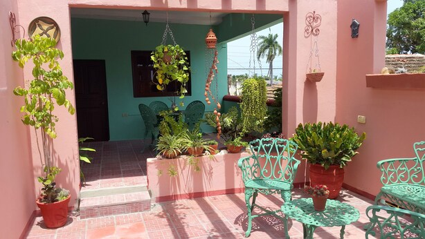 A patio with potted plants, a hanging wind chime, and green metal chairs. - Hostal Restaurante La Rosa (Trinidad)