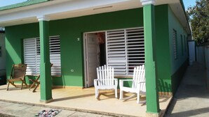 A green building with white shutters, a door, and two white chairs outside. - Villa Isabel y Luisito (Viñales)