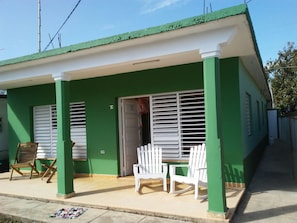 A green building with white shutters, a door, and two white chairs outside. - Villa Isabel y Luisito (Viñales)