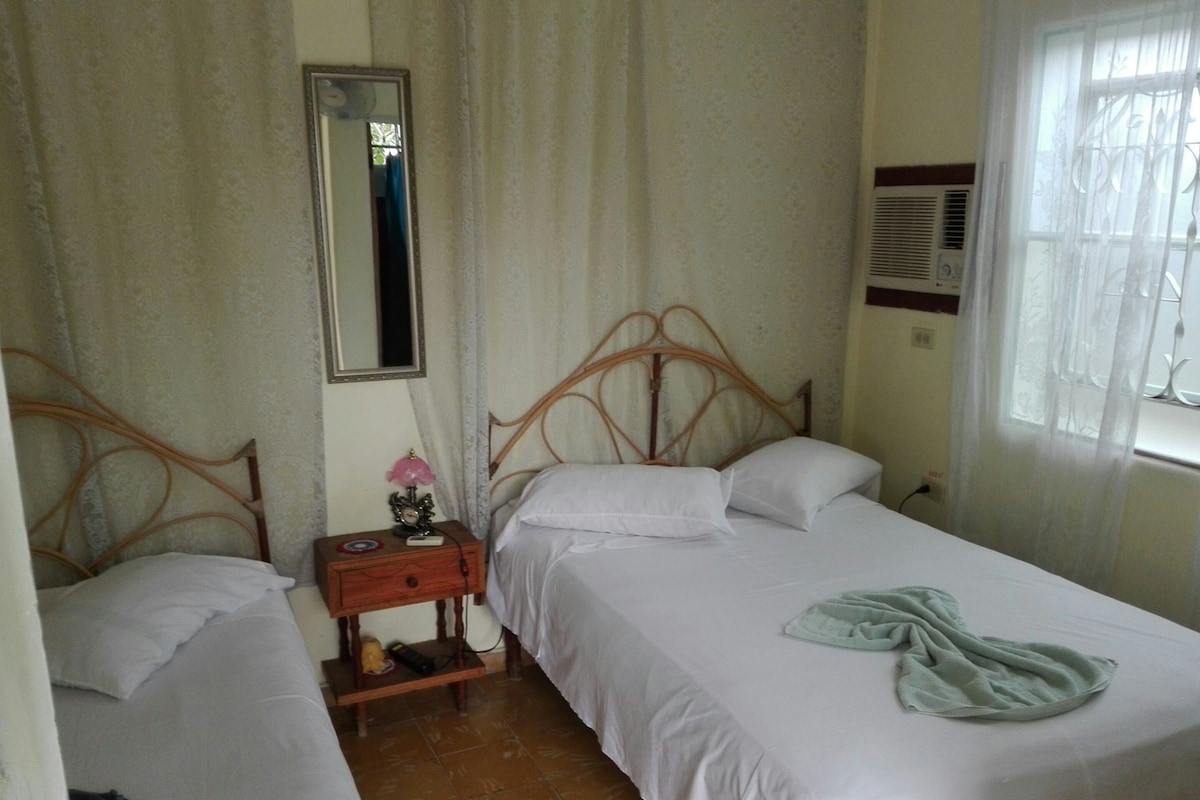 A bedroom with two single beds, a nightstand with a lamp, a mirror, and a window with curtains.