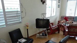 A living room with a television on a stand, a black sofa, a red chair, and a small table with a vase of flowers. - Villa Isabel y Luisito (Viñales)