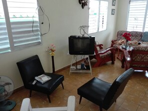 A living room with a television on a stand, a black sofa, a red chair, and a small table with a vase of flowers. - Villa Isabel y Luisito (Viñales)