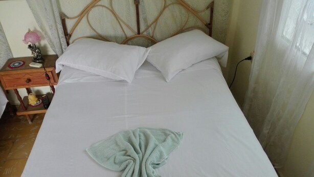 A neatly made bed with white linens, a folded towel, and a wooden headboard. - Villa Isabel y Luisito (Viñales)