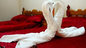 Uma cama com roupa de cama vermelha e uma toalha branca dispostas em formato de coração.