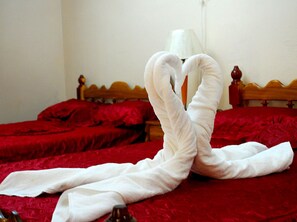 Ein Bett mit roter Bettwäsche und einem weißen Handtuch, kunstvoll zu einem Herzen geformt.