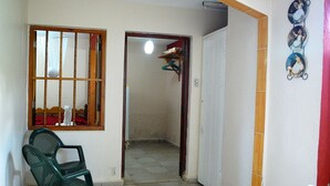 Quarto com uma cadeira, janela com grades, porta para outro cômodo e parede com um quadro.