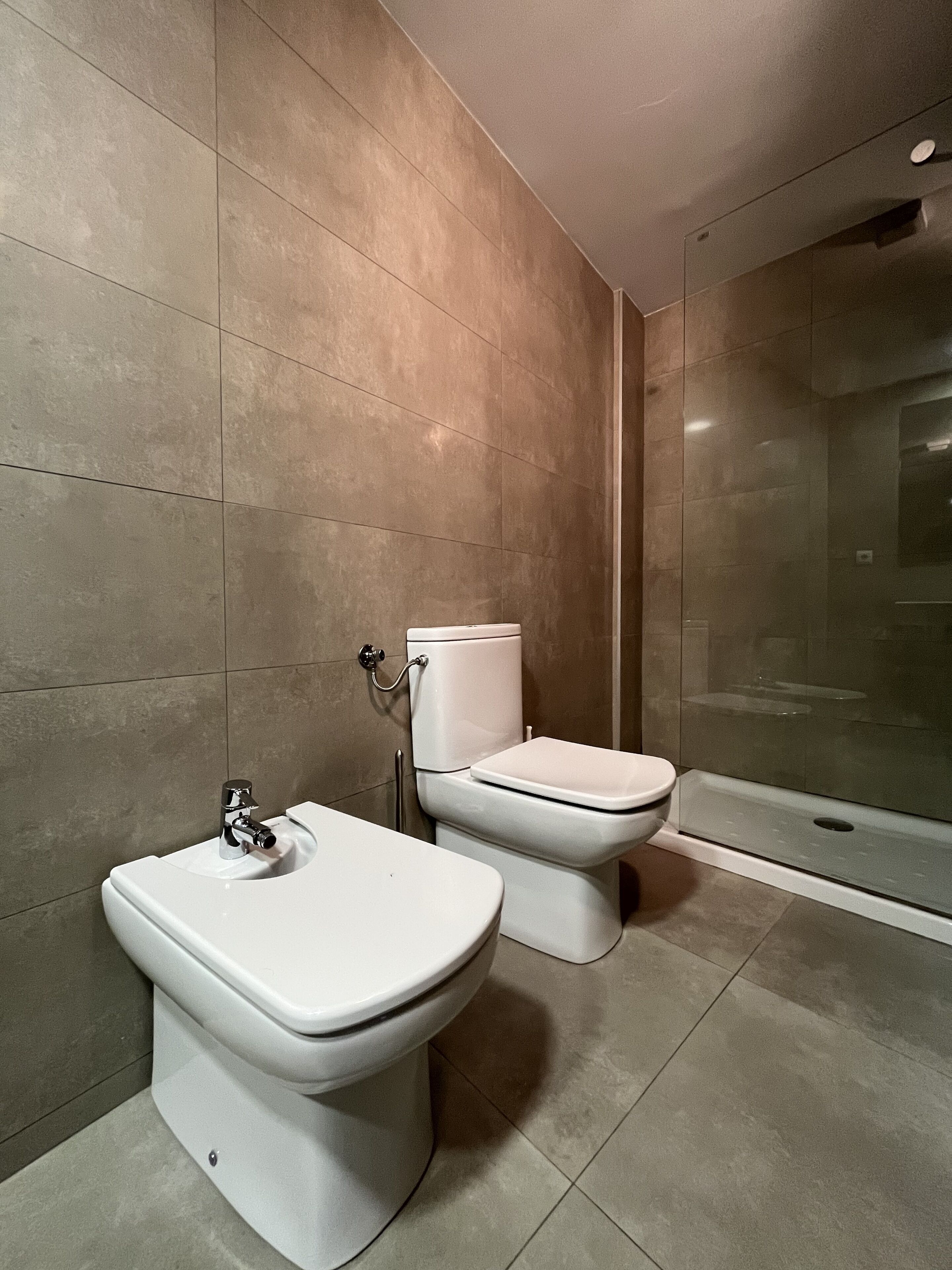Un baño moderno con inodoro, bidé y cabina de ducha de vidrio.