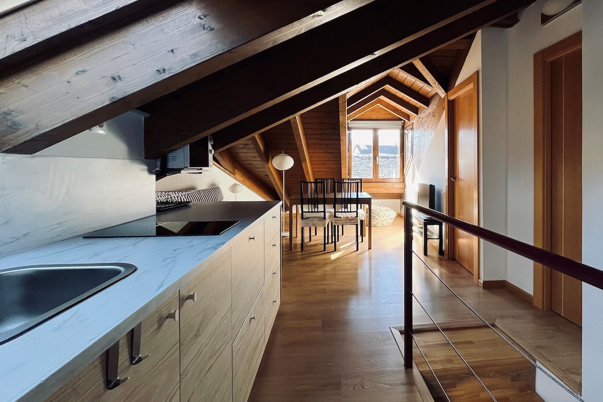 Een moderne keuken met een groot kookeiland, houten balken en uitzicht op een eetgedeelte.