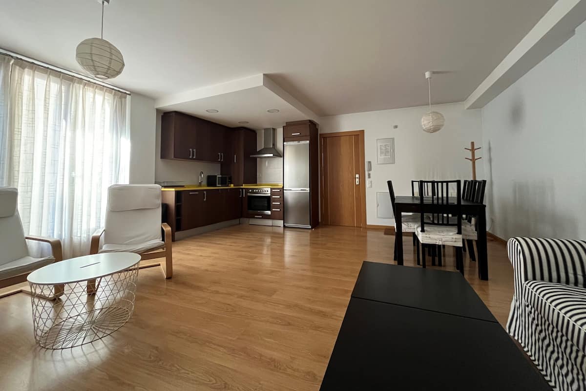 Een moderne woonkamer met een eethoek, houten vloeren en een keuken op de achtergrond.