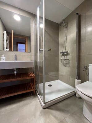 A modern bathroom with a glass-enclosed shower, a white sink with a wooden vanity, and a toilet. - Casa Damián del Baile Apartamentos (Benasque)