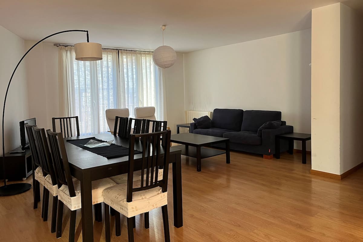 Een moderne woonkamer met een eethoek, met een houten eettafel, stoelen, een bank en een salontafel.