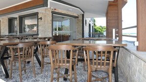 Un espace extérieur aménagé pour les repas, avec des tables et des chaises en bois, des murs en pierre et une vue sur la mer.
