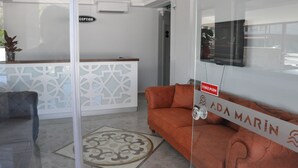 Un espace d’accueil comprenant un comptoir de réception, un canapé, un tapis à motifs et un téléviseur fixé au mur.
