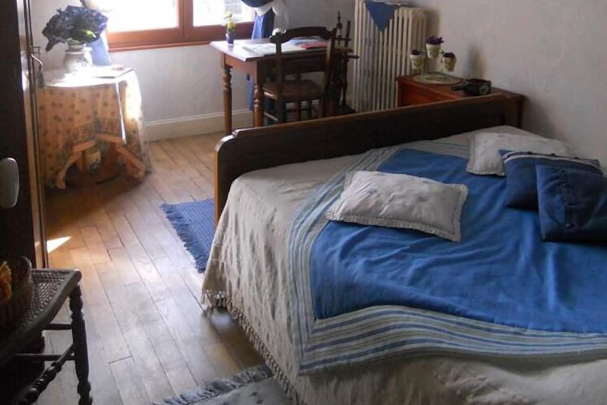 A bedroom with a bed, a desk, a chair, a bookshelf, and a window with curtains.