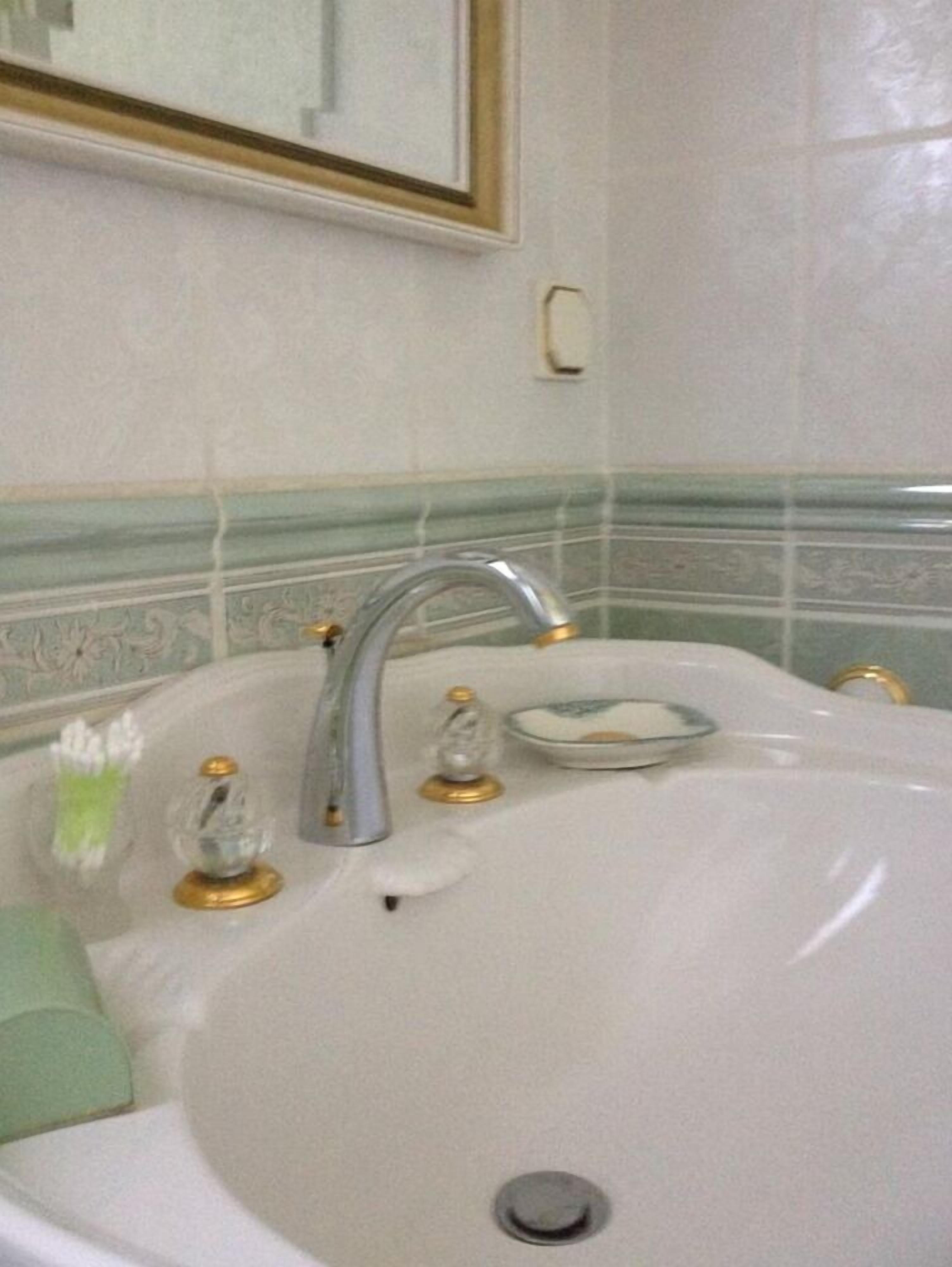 Une salle de bain avec un grand lavabo blanc, un miroir au-dessus et une bordure décorative en carreaux.
