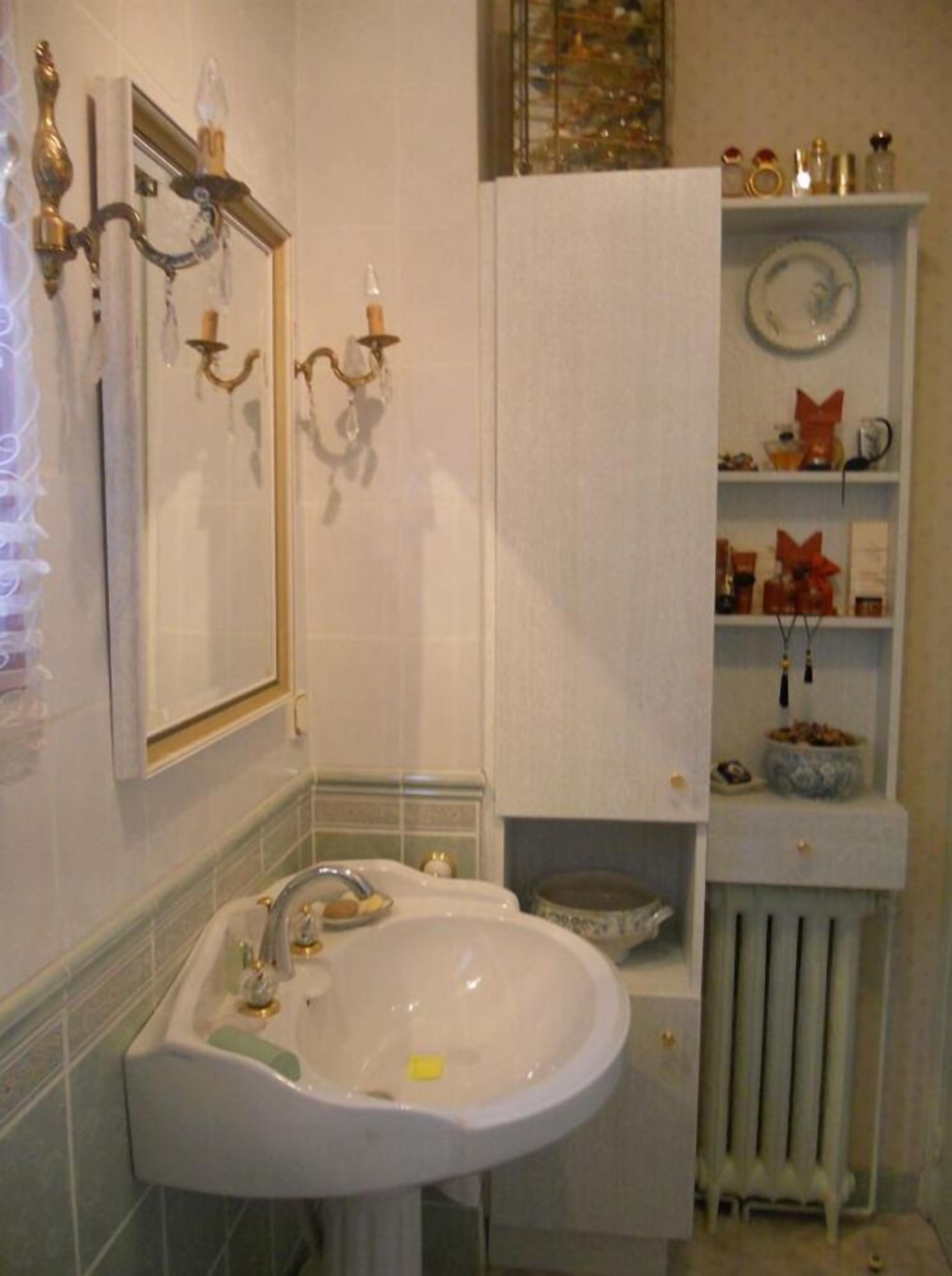 Un baño con lavamanos blanco, dos apliques de pared, un espejo y un radiador.