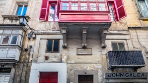 A building facade with a red door, a plaque reading "JOHN GALEA," and a balcony with a metal railing. - Valletta Kampnar City Living (Valletta)