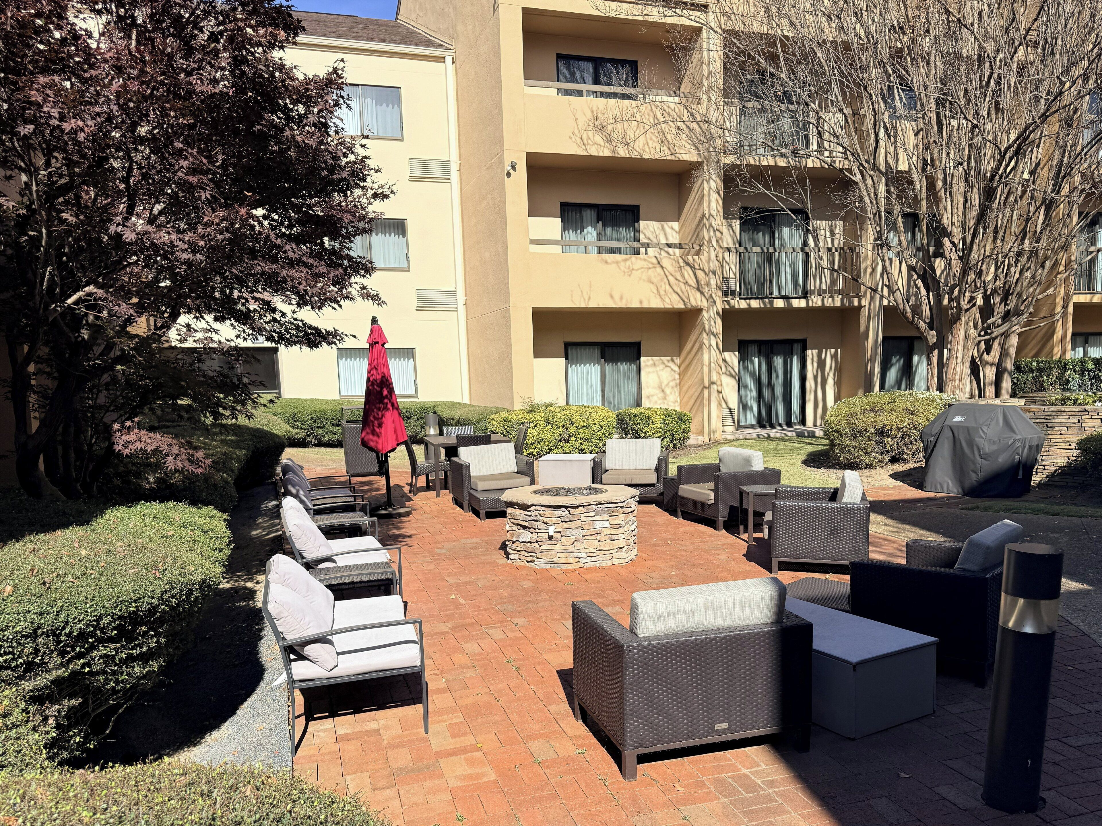 An outdoor seating area with wicker furniture, a red umbrella, and a stone fire pit.