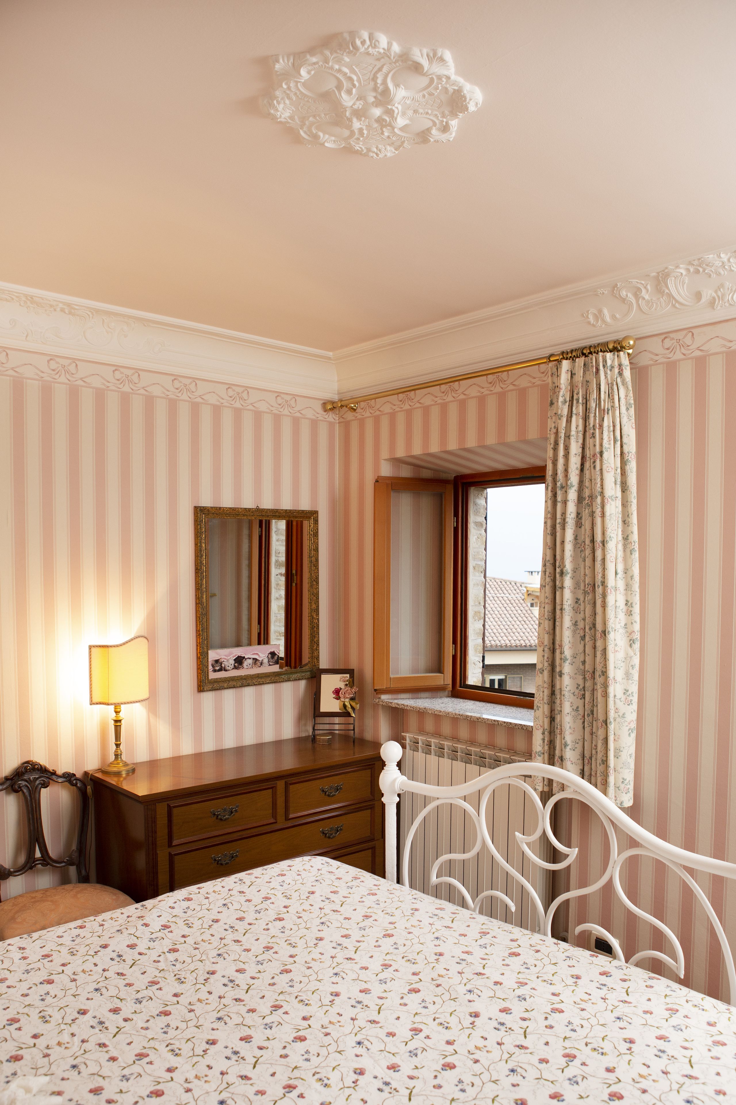 Ein Schlafzimmer mit Bett, Kommode, Spiegel und Fenster mit Vorhängen.
