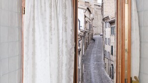 A narrow hallway with a view of a cobblestone street through an open door. A basket with towels and a decorative item is placed on the floor. - B&B Porta Marina (Recanati)