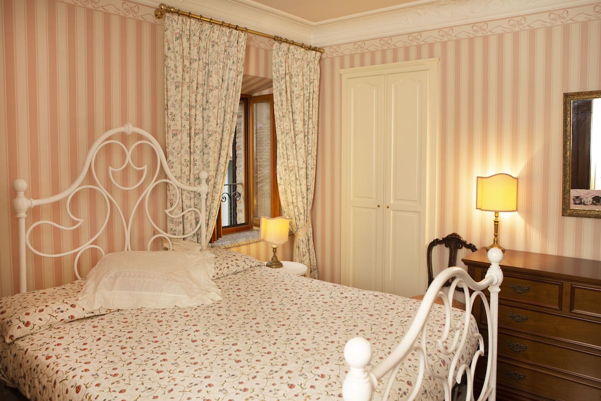 A bedroom with a bed, curtains, a lamp, a dresser, and a door.