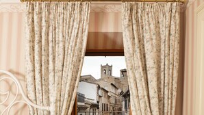 A bedroom with a bed, a nightstand, a lamp, a window with curtains, and a view of a street scene. - B&B Porta Marina (Recanati)