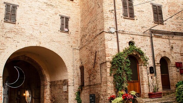 A historic building with a brick facade, arched entrance, and potted plants. - B&B Porta Marina (Recanati)