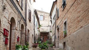 A narrow alleyway with brick buildings, a cobblestone path, and lush greenery. - B&B Porta Marina (Recanati)