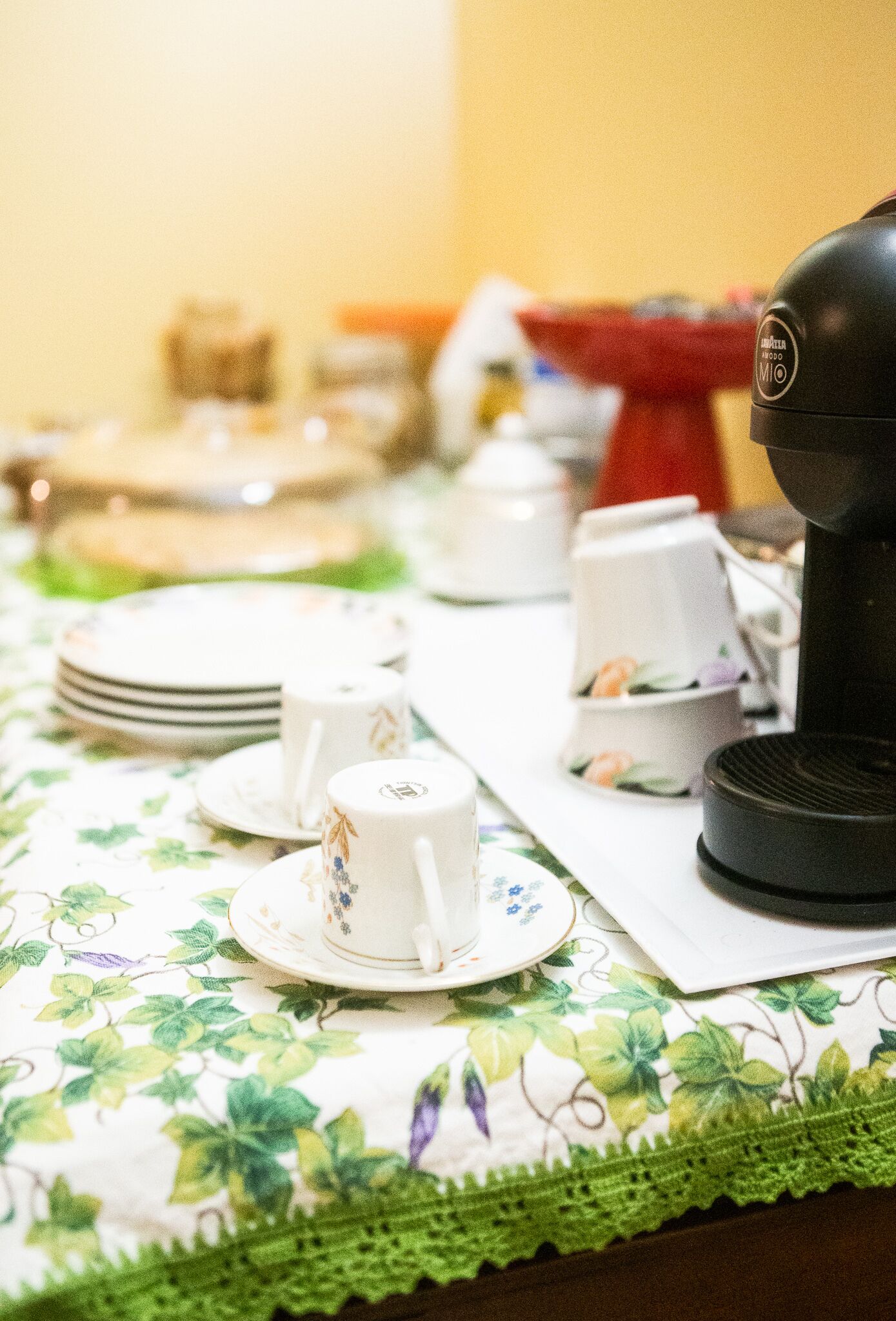 A table set with plates, cups, and a coffee maker, covered by a floral tablecloth.