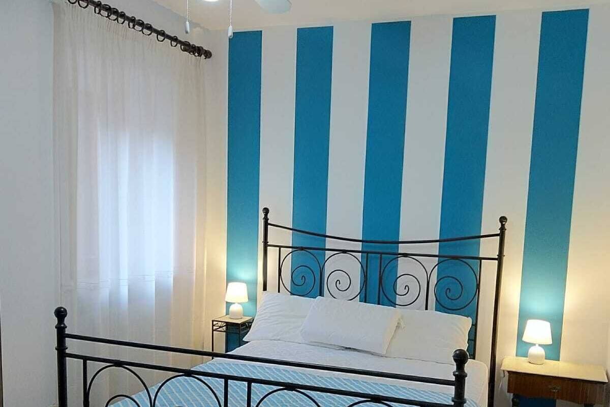 A bedroom with a bed, a ceiling fan, a nightstand with a lamp, and a wooden table.
